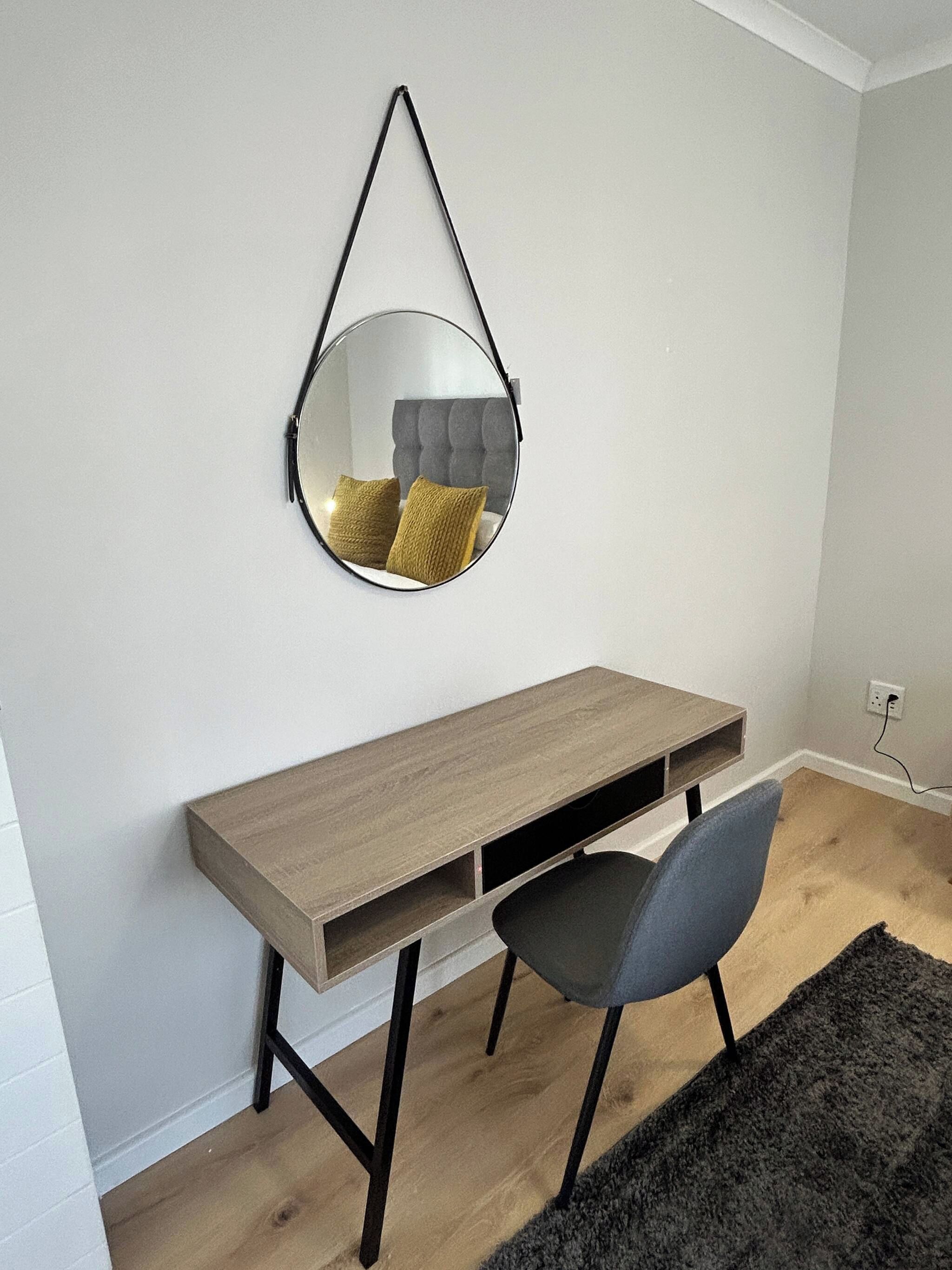A room with a desk, chair, and a hanging mirror.
