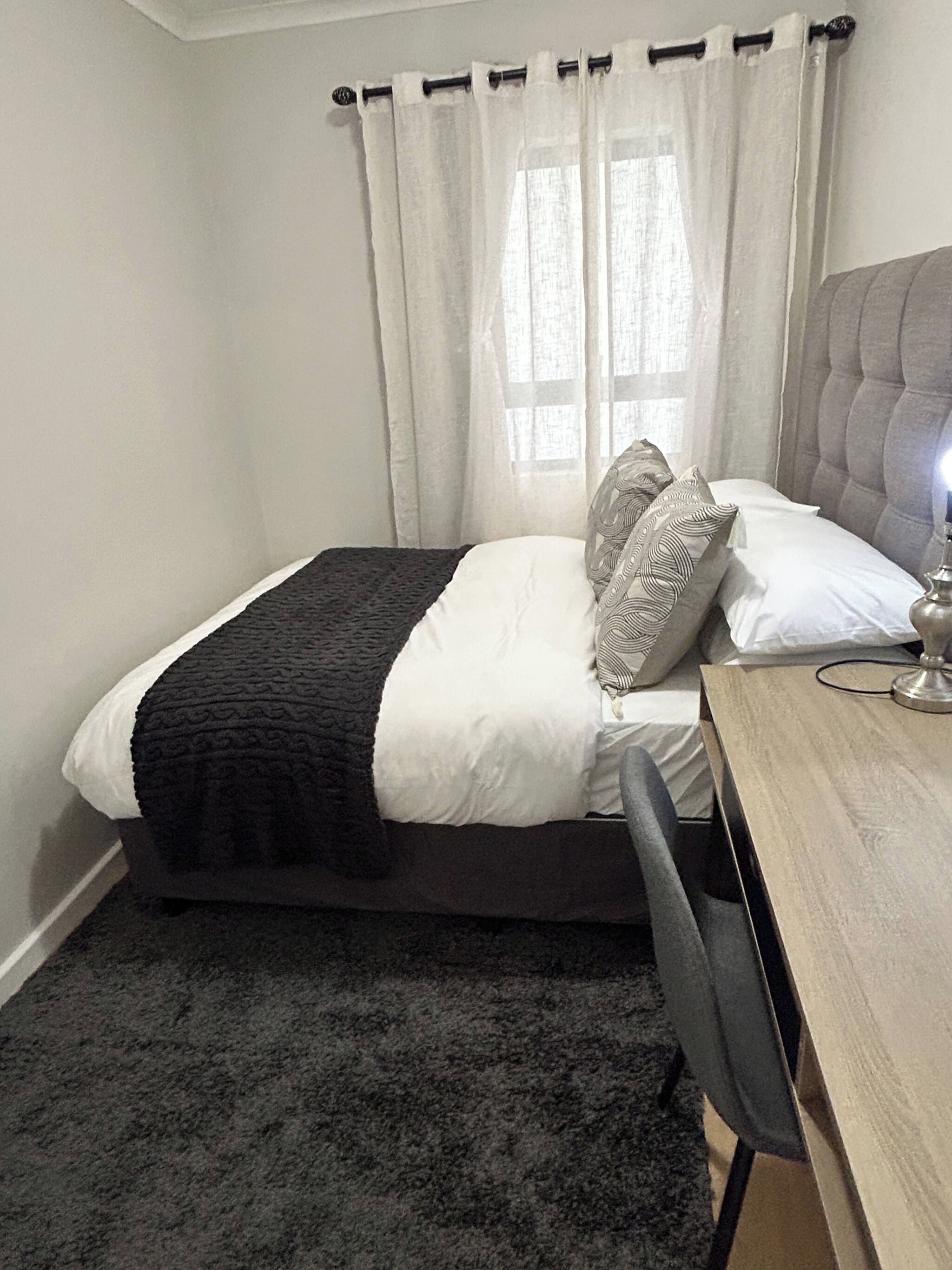 A bedroom with a bed, a desk, a chair, and a window with curtains.