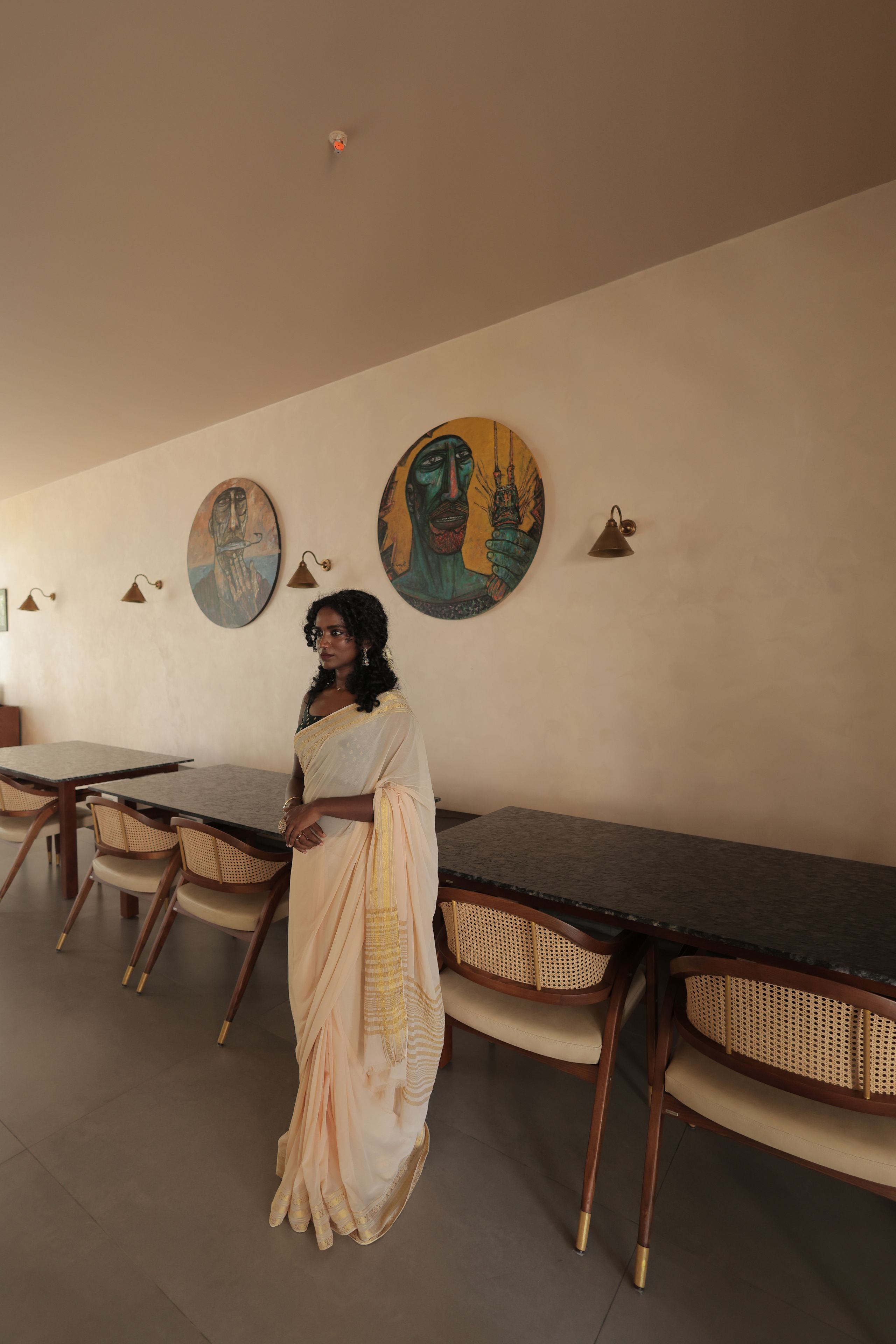 A person in traditional attire standing in a room with a long table and chairs, with artwork on the walls.