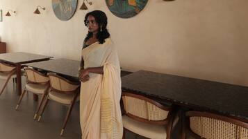 A person in traditional attire standing in a room with a long table and chairs, with artwork on the walls.