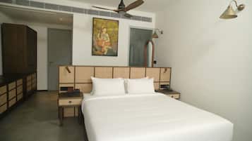 A hotel room with a bed, a nightstand, a painting, a ceiling fan, and a wall-mounted lamp.