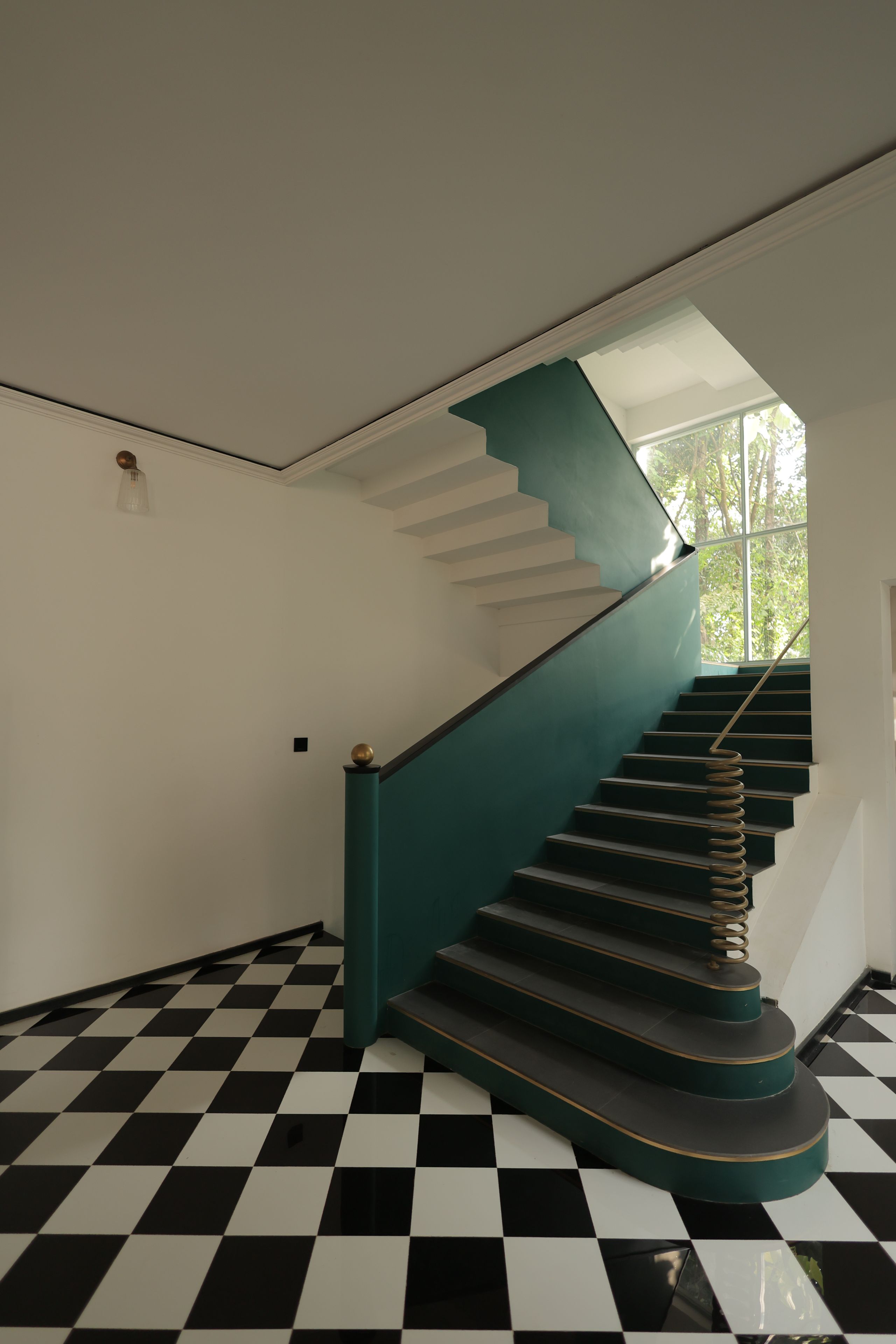 Una escalera con piso a cuadros, paredes blancas y barandilla color turquesa.
