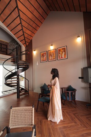 A spacious room with a spiral staircase, wooden flooring, and artwork on the walls. - One Kochi (Nedumbassery)