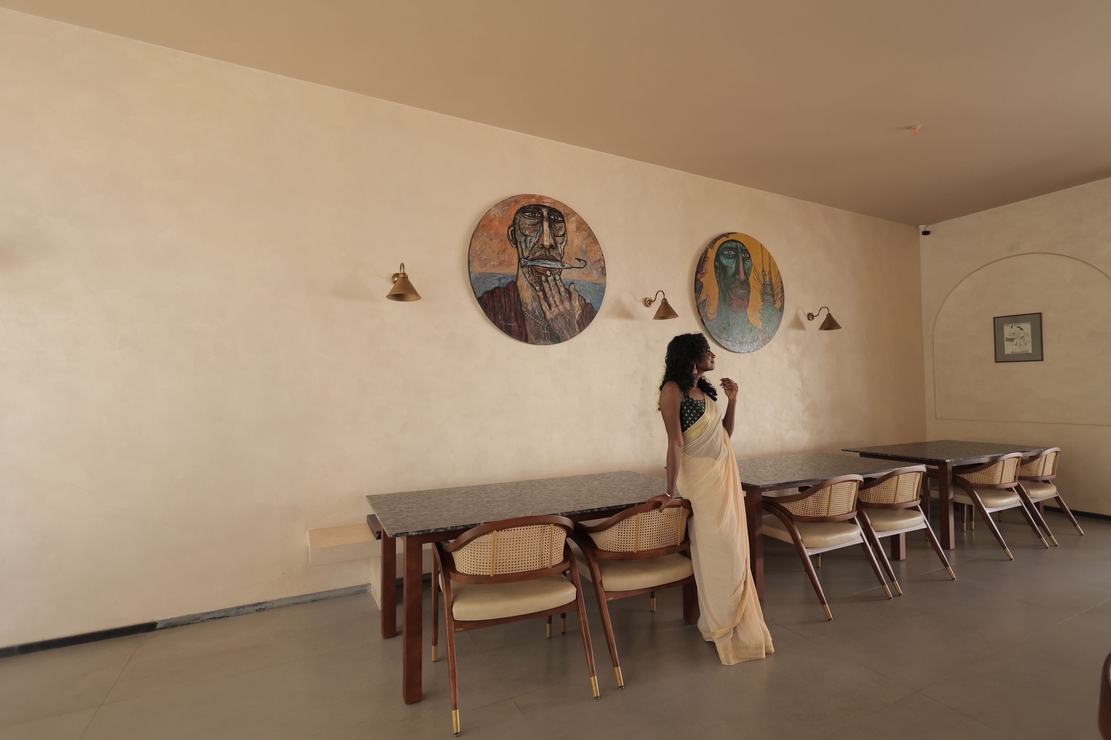 Un comedor con una mesa y sillas, una persona vestida con traje tradicional, y dos cuadros colgados en la pared.