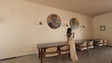 Un comedor con una mesa y sillas, una persona vestida con traje tradicional, y dos cuadros colgados en la pared.