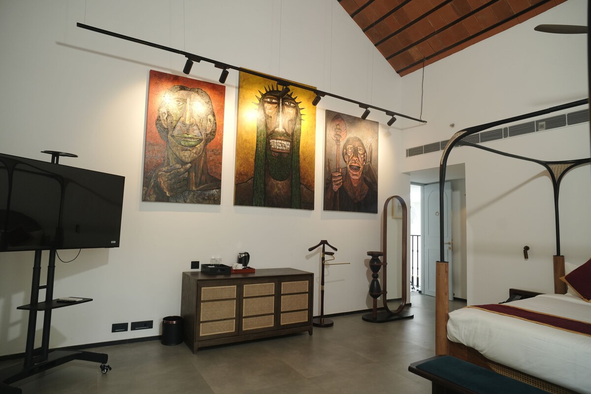 A room with a bed, a television, a cabinet, and three paintings on the wall.