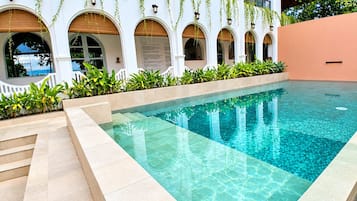Una piscina con agua cristalina, rodeada por un edificio blanco con ventanas de arco y plantas colgantes.