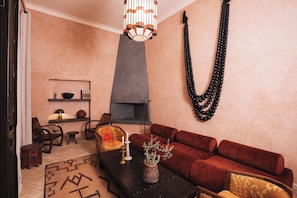 A cozy living room with a fireplace, a red sofa, a coffee table with a vase, and a chandelier. - Fabulous 4-bedroom Riad with Pool in vibrant Marrakech (Marrakech)