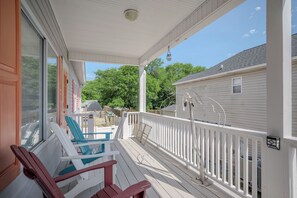 A covered porch with two chairs, a small table, and a white railing. - Barefoot Bungalow: Private Pool, Golf Cart Rental (Oak Island)