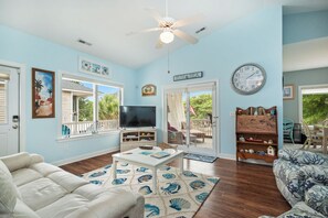 Ein Wohnzimmer mit Deckenventilator, Fernseher, großem Fenster und einer Wanduhr.