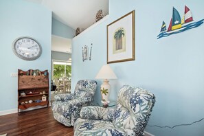 A room with a clock, a framed picture, a lamp, and a chair with a floral pattern. - Barefoot Bungalow: Private Pool, Golf Cart Rental (Oak Island)