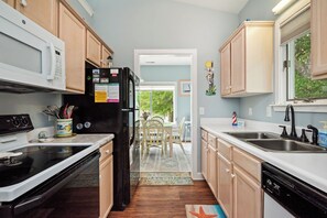 A kitchen with wooden cabinets, a black refrigerator, a microwave, a stove, and a sink. - Barefoot Bungalow: Private Pool, Golf Cart Rental (Oak Island)