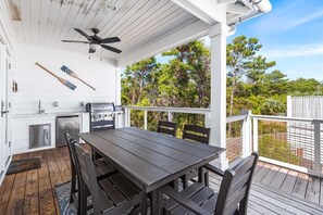 A covered outdoor dining area with a table and chairs, a ceiling fan, and a view of the surrounding trees. - Sunkissed & Salty (Panama City Beach)