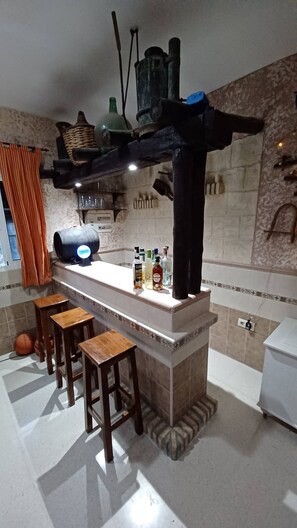A kitchen with a bar area, stools, a countertop with bottles, and a hanging light fixture. - VILLA WITH PRIVATE POOL IN SANLUCAR DE BARRAMEDA - VILLA MI DESEO (Sanlúcar de Barrameda)