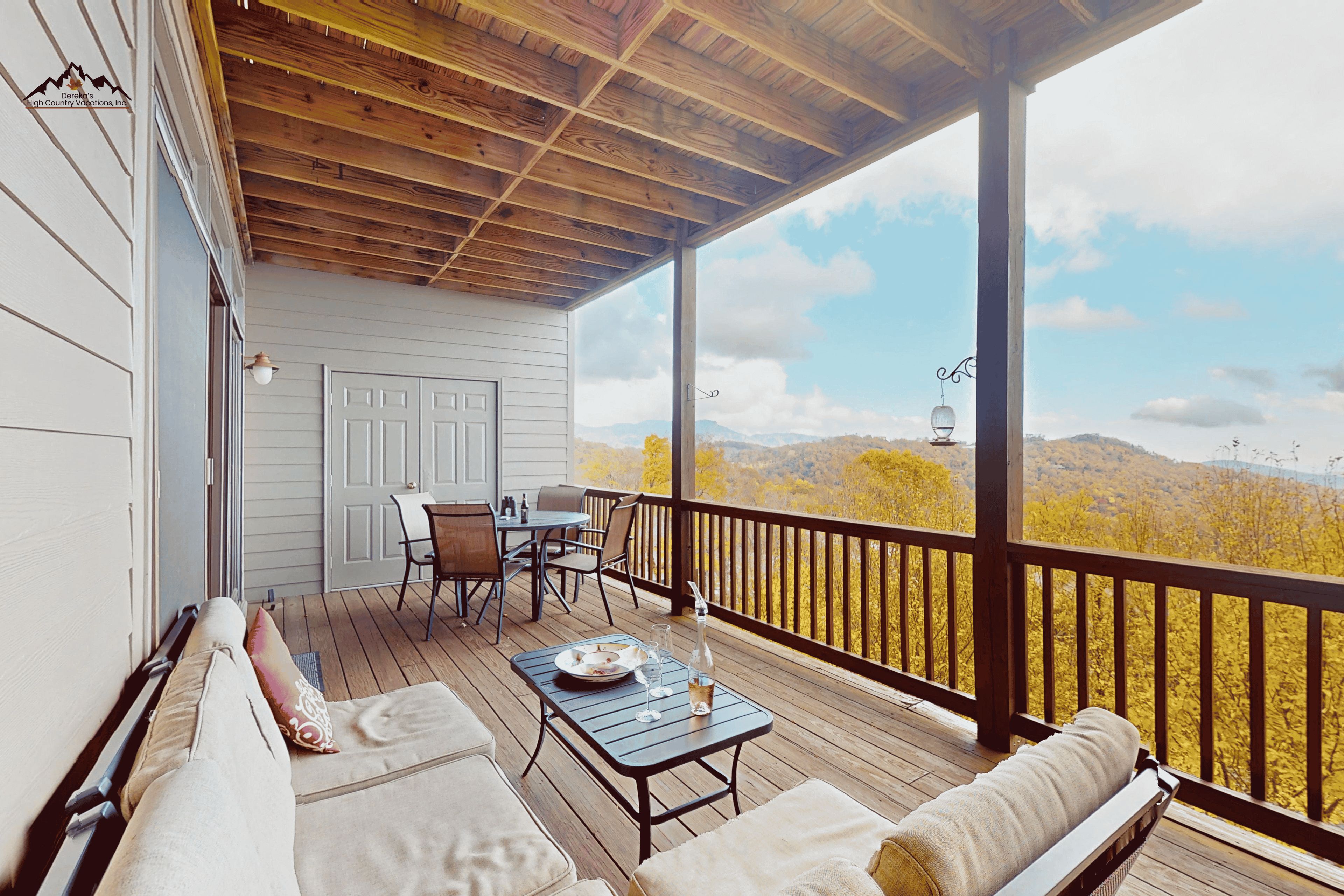 A covered outdoor area with a wooden deck, a table with chairs, and a view of a mountainous landscape.
