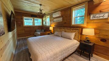 A wooden cabin bedroom with a large bed, two bedside tables, a TV, and a chandelier.