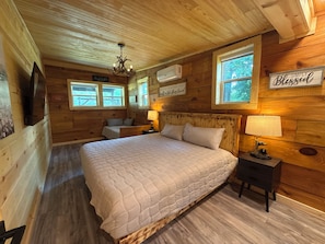 A wooden cabin bedroom with a large bed, two bedside tables, a TV, and a chandelier. - The little cabin retreat (Bowdon)