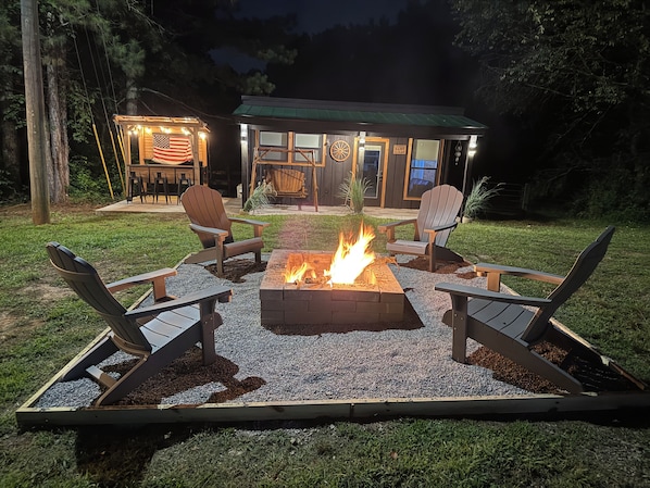 An outdoor seating area with a fire pit and Adirondack chairs. - The little cabin retreat (Bowdon)