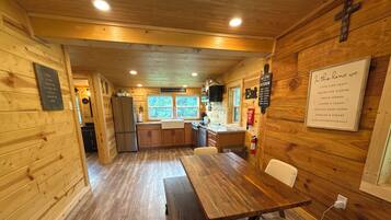 A wooden interior with a dining table, chairs, a kitchen area, and a wall-mounted sign.