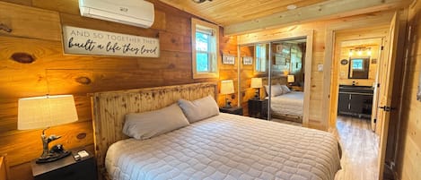 A wooden cabin bedroom with a bed, bedside lamps, a mirror, and a sign on the wall.