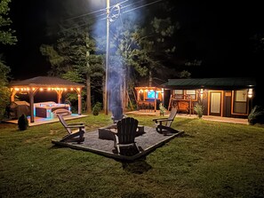 An outdoor patio area with seating and a hot tub, surrounded by a covered structure with string lights.