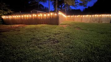 Une cour clôturée, avec une clôture en bois et des guirlandes lumineuses.