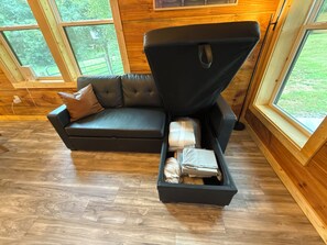 A modern living room with a sectional sofa, a built-in storage bench, and large windows offering a view of the outdoors.