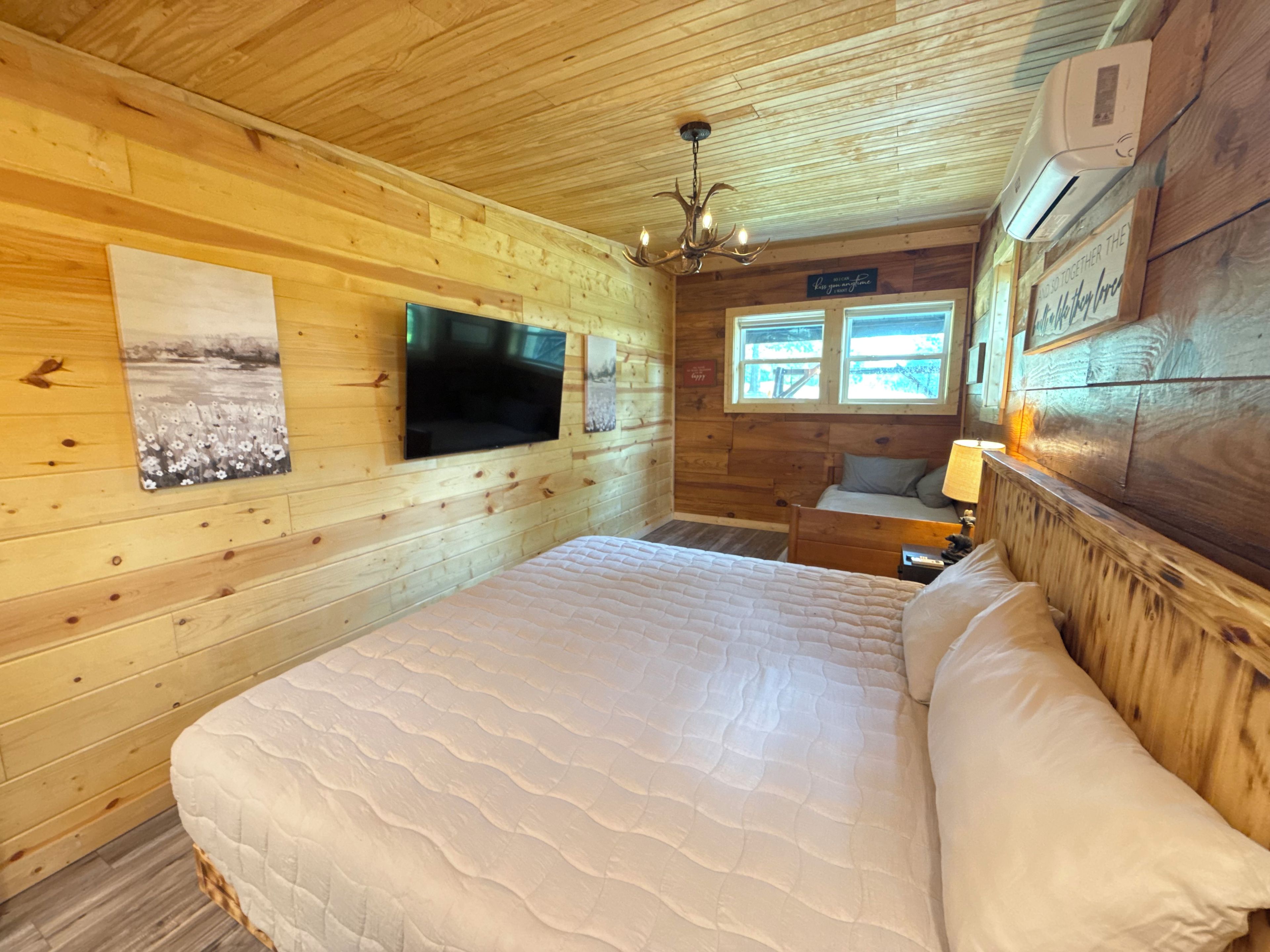 Dormitorio de cabaña de madera con cama, televisor montado y candelabro.