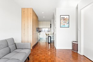 A modern apartment with a grey sofa, wooden flooring, a kitchen with white cabinets, and a dining area with chairs. - GuestReady - Cozy Porto Retreat with Balcony (Porto)