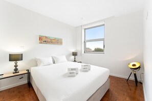 A hotel room with a large bed, two bedside tables, a window, and a wall-mounted artwork. - GuestReady - Cozy Porto Retreat with Balcony (Porto)