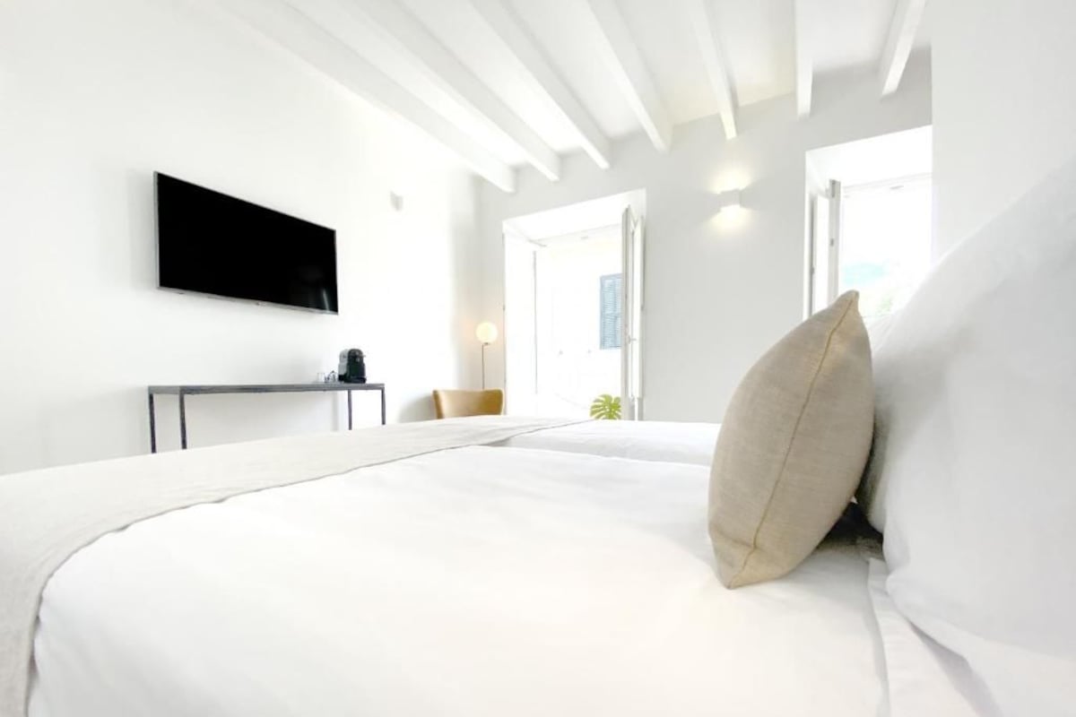 A modern hotel room with a bed, a flat-screen TV, a bedside table, and a window.