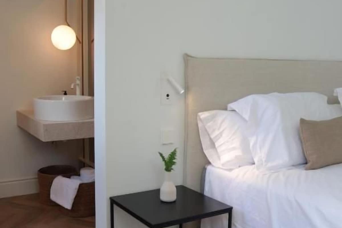 A hotel room with a bed, bedside table, and a small bathroom area with a sink and mirror.
