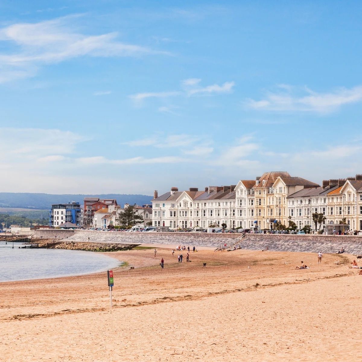 A coastal hotel with multiple stories, a sandy beach in front, and a clear sky.