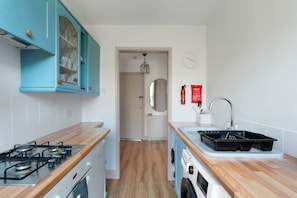 A compact kitchen with a gas stove, a washing machine, and a sink. - The Exmouth Nook, Walk to Beach, Parking Nearby (Exmouth)