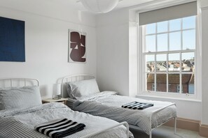 A bedroom with two beds, a large window, and a view of buildings outside. - The Exmouth Nook, Walk to Beach, Parking Nearby (Exmouth)