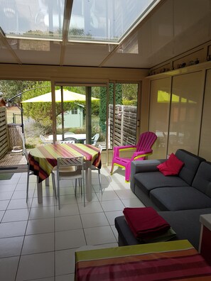 Una habitación iluminada por el sol con una mesa de comedor, sillas, un sofá y una puerta corrediza de vidrio que da a un espacio exterior.