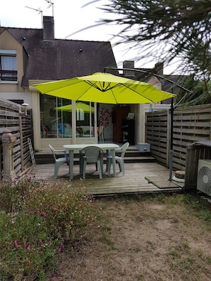 A patio with a table and chairs, a yellow umbrella, and a wooden deck. - House in a complex with a swimming pool in the summer, 900 meters from the beach (Batz-sur-Mer)