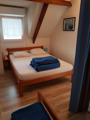 A bedroom with a wooden bed, a window with blinds, a picture on the wall, and a blue curtain. - House in a complex with a swimming pool in the summer, 900 meters from the beach (Batz-sur-Mer)