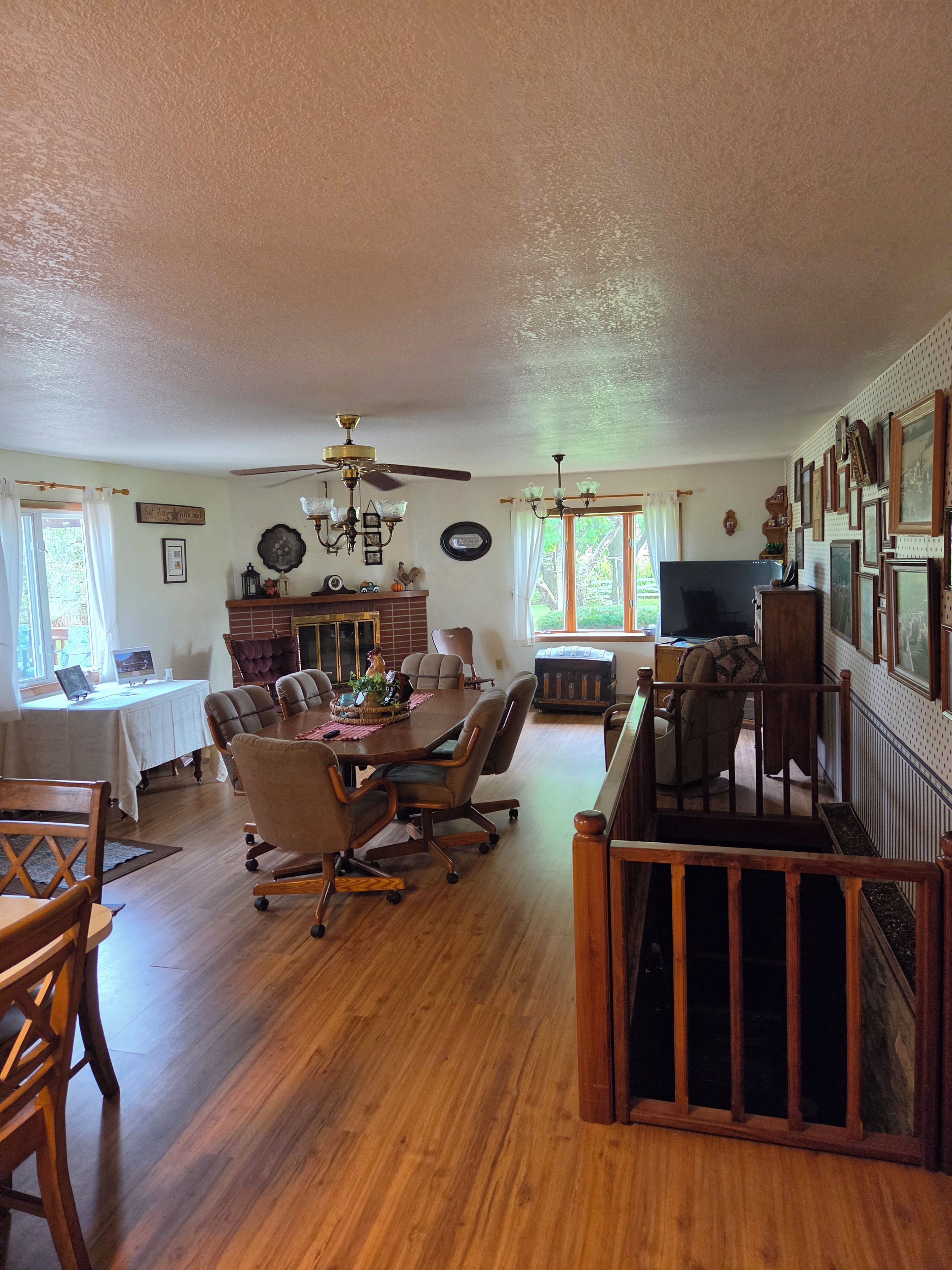 A spacious living room with a dining area, wooden floors, ceiling fans, and a fireplace.