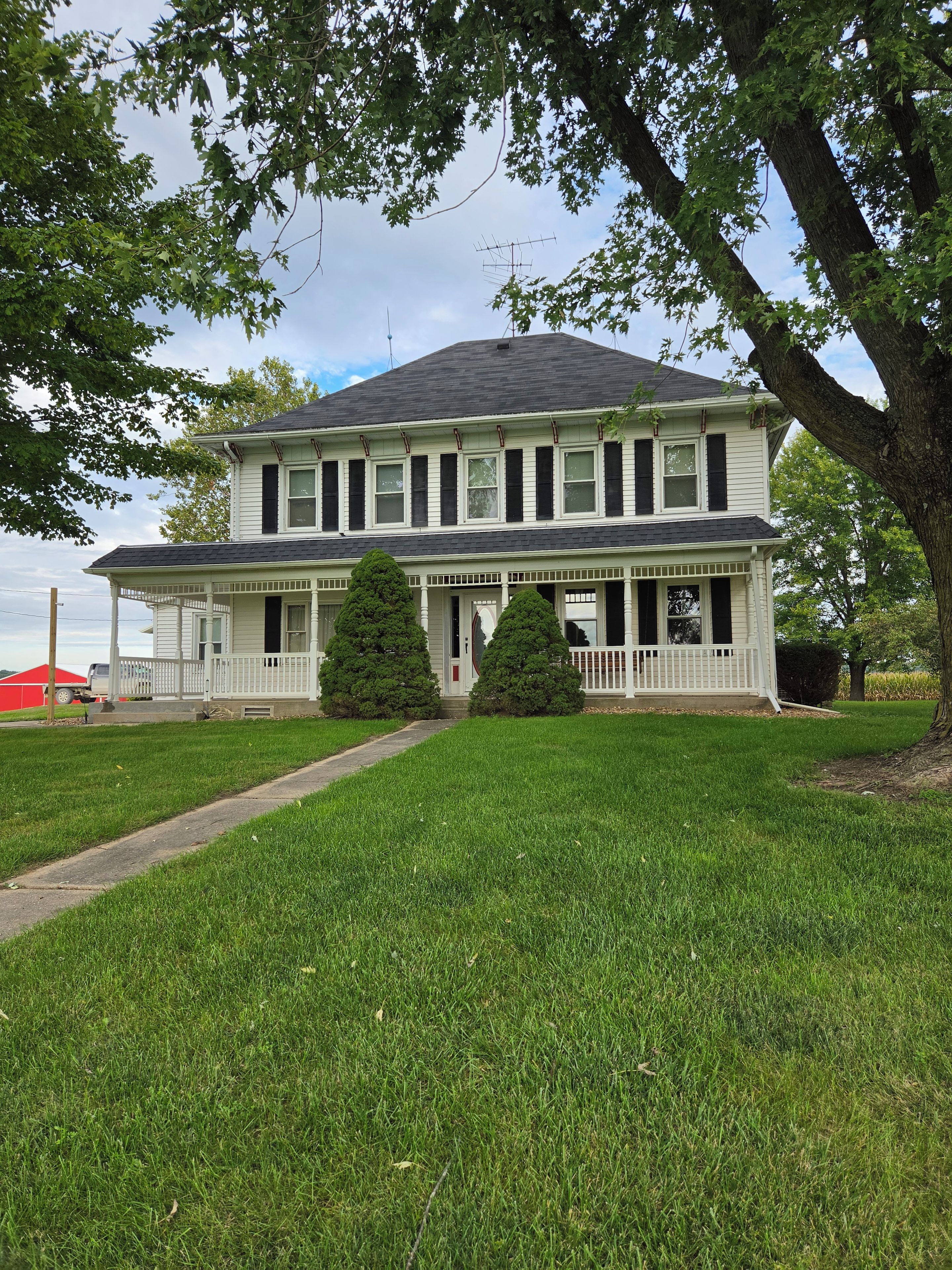 A two-story house with a porch, a lawn, and a large tree in front.