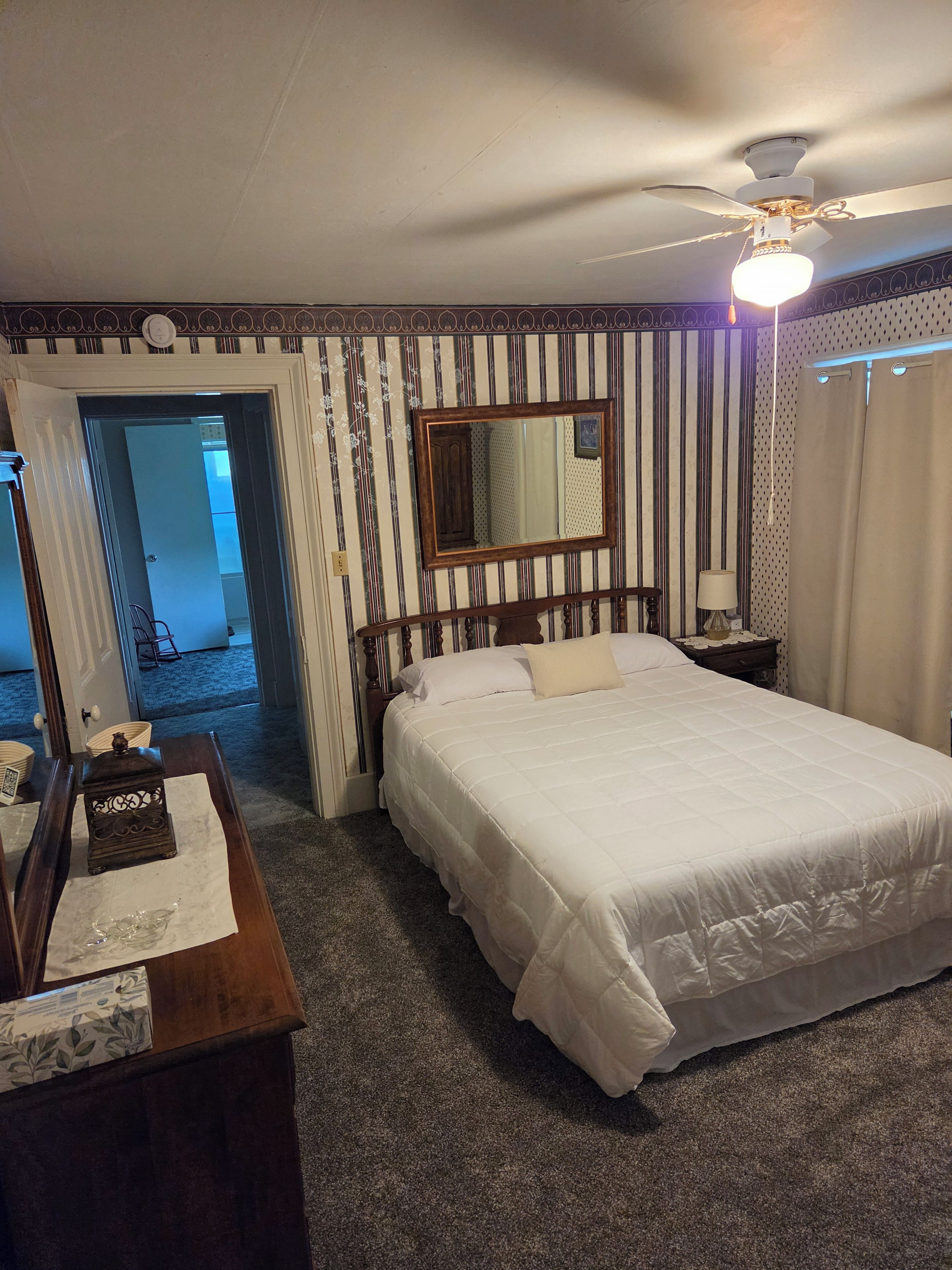 A hotel room with a large bed, a ceiling fan, a mirror, and a door leading to another room.