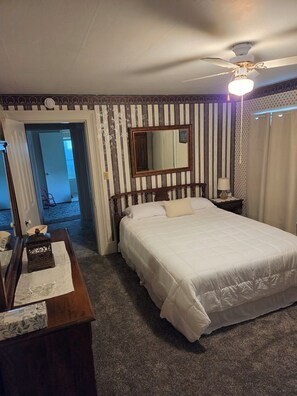 Une chambre d’hôtel avec un grand lit, un ventilateur de plafond, un miroir et une porte donnant sur une autre pièce.