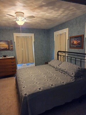 Ein Schlafzimmer mit einem Bett, einem Schminktisch, einem Deckenventilator und Vorhängen.