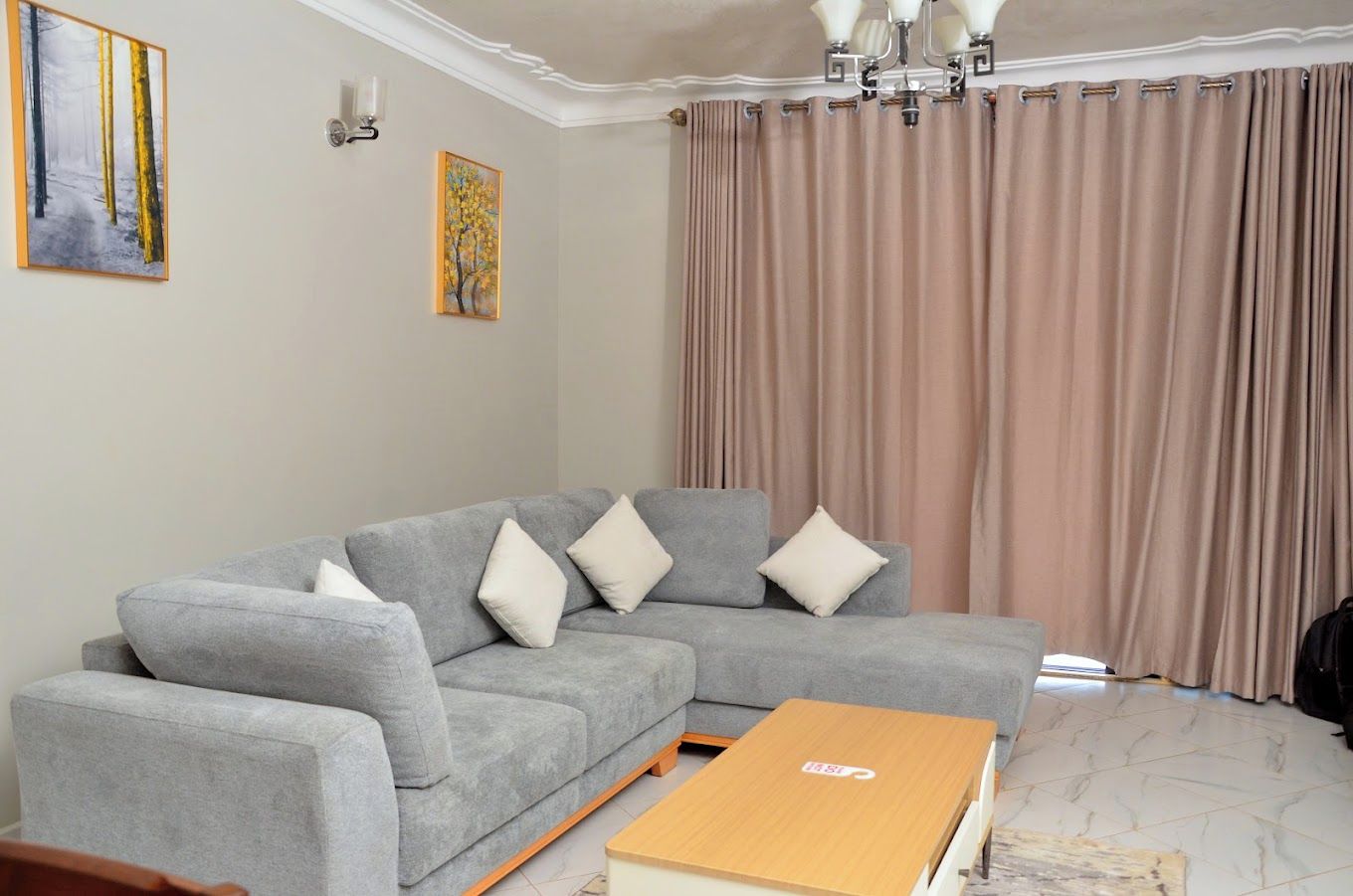 Una sala de estar con un sofá seccional gris, una mesa de centro de madera y un ventanal con cortinas color beige.