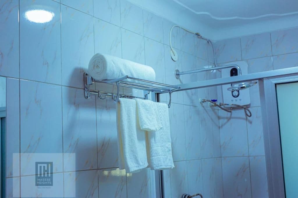 Baño con azulejos de mármol blanco, un toallero con una toalla enrollada y dos toallas, un cabezal de ducha y un panel de control.