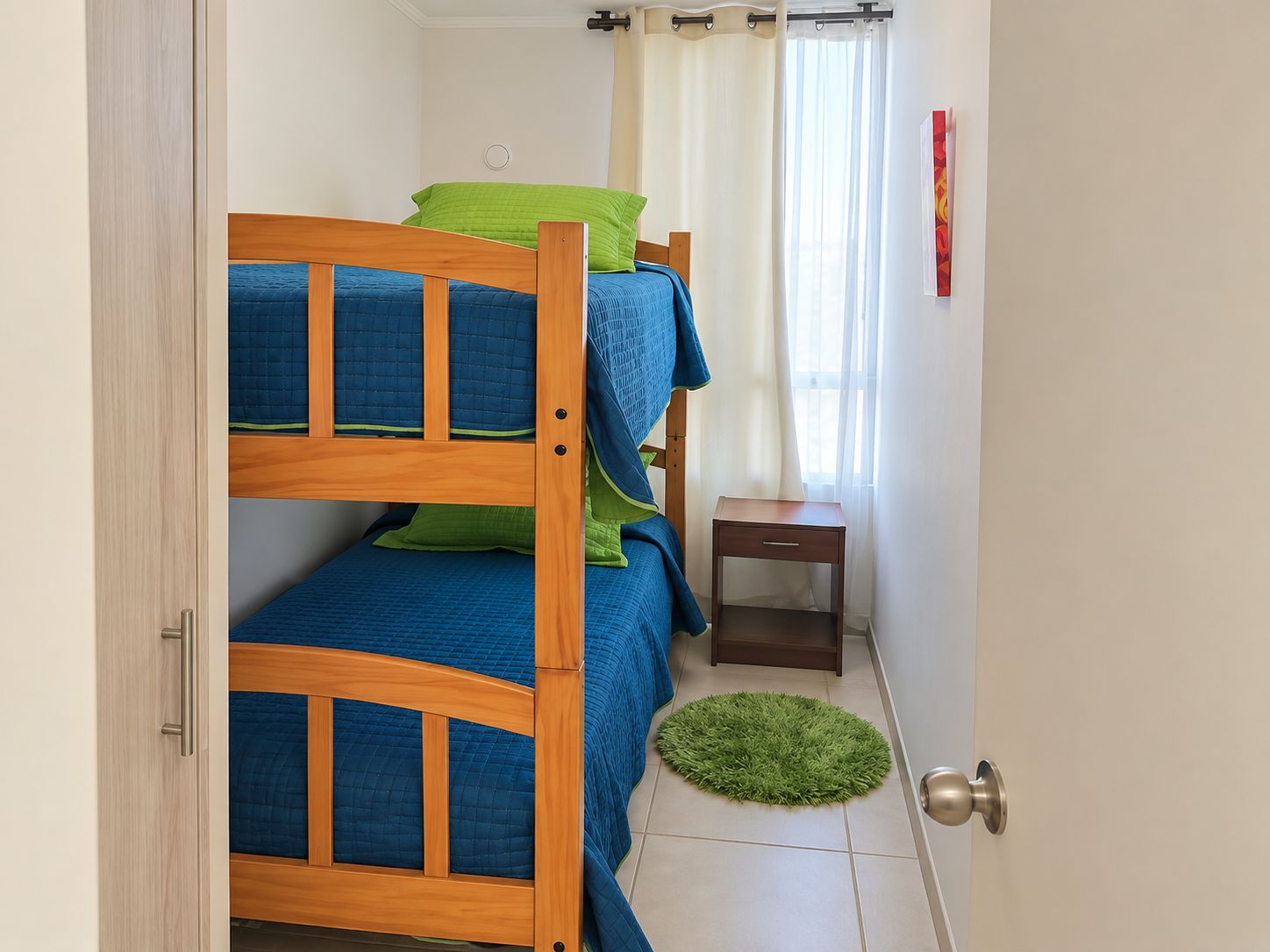 A small, well-lit room with a bunk bed, a bedside table, and a green rug.