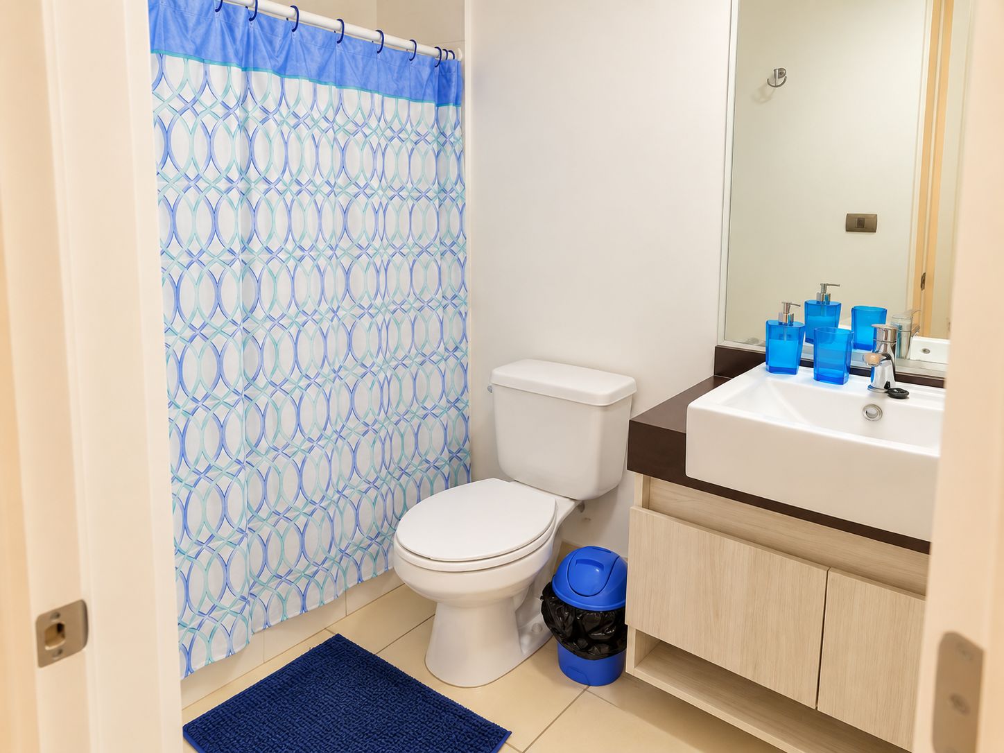 Un baño con inodoro, lavamanos y cortina de ducha estampada con un diseño geométrico.
