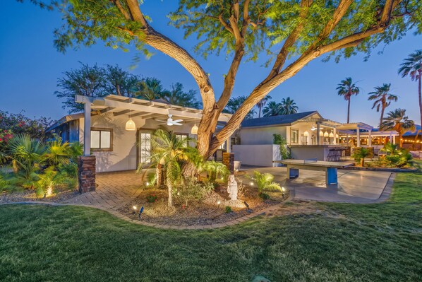 A modern house with a covered patio, a large tree, and a well-maintained lawn.