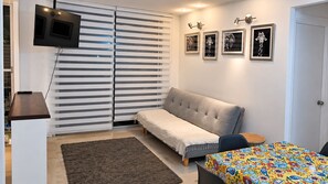 Una habitación con sofá, una mesita, televisor integrado en una puerta corredera y cuadros en la pared.