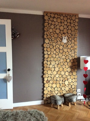 A room with a wall decorated with stacked logs, a small stool, and a heart-shaped decoration.